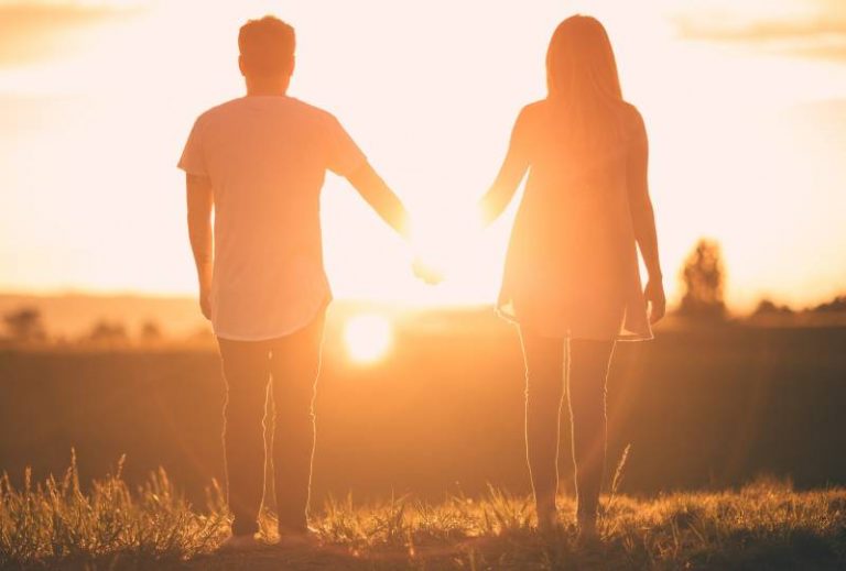 un homme et une femme se tenant la main face au coucher du soleil