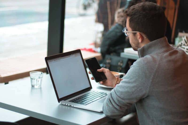 Homme assis près d'une table avec un ordinateur portable et un smartphone près de la fenêtre