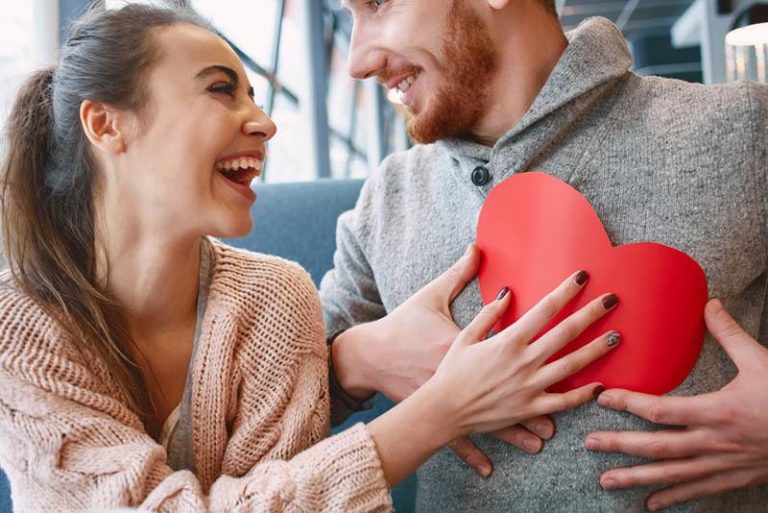 Une femme souriante donne à son homme une forme de coeur en papier