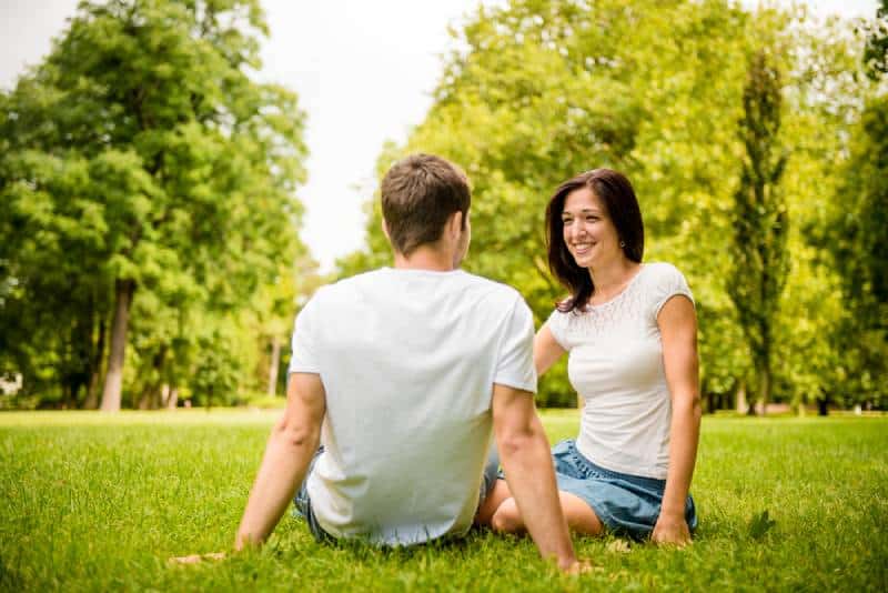 Jeune couple heureux discutant ensemble en plein air - assis sur l'herbe