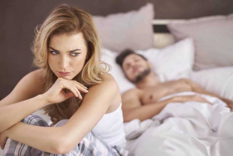 femme réfléchie assise sur le lit alors que l'homme est couché