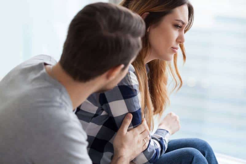 Le mari aimant réconforte la femme offensée, la caresse et l'embrasse par derrière