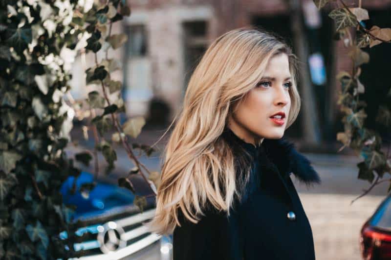 femme sérieuse avec un manteau noir à côté de vignes vertes
