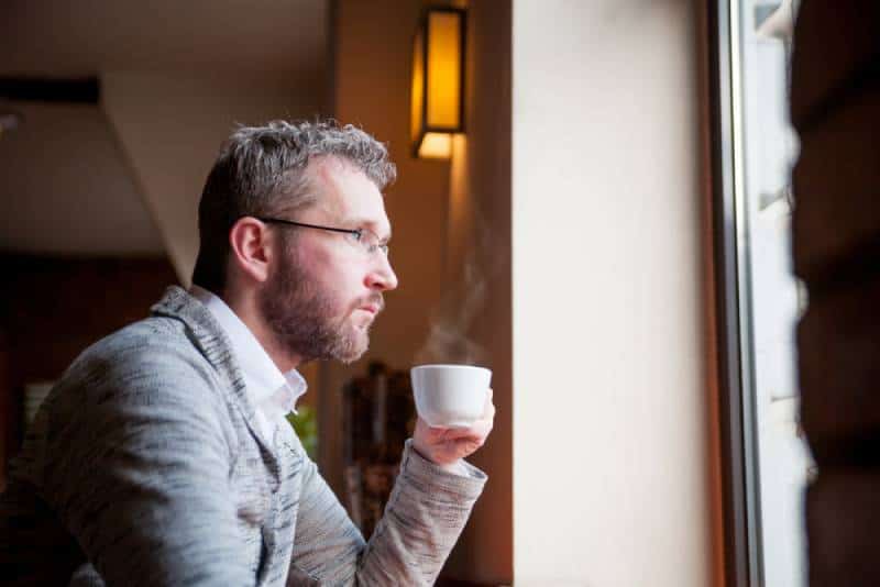Un homme attentionné qui boit un café au café et regarde par la fenêtre