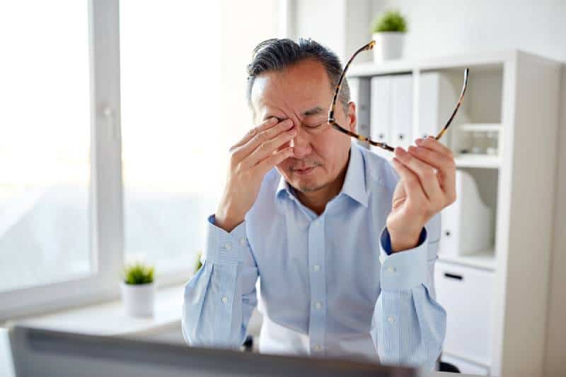 Un homme d'affaires fatigué avec des lunettes et un ordinateur portable qui se frotte les yeux au bureau
