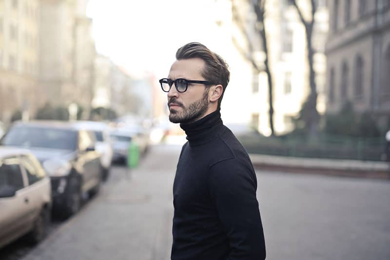 Un homme portant des lunettes et un sweat-shirt noir se tient à l'extérieur