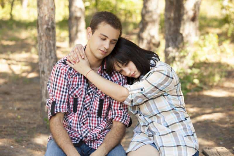 Un jeune couple d'adolescents tristes dans un parc vert.