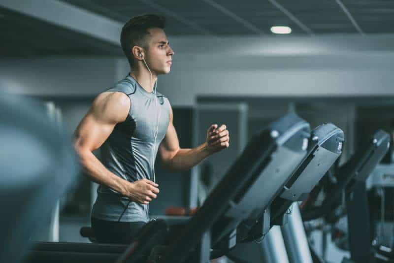Un jeune homme en tenue de sport court sur un tapis roulant à la salle de sport