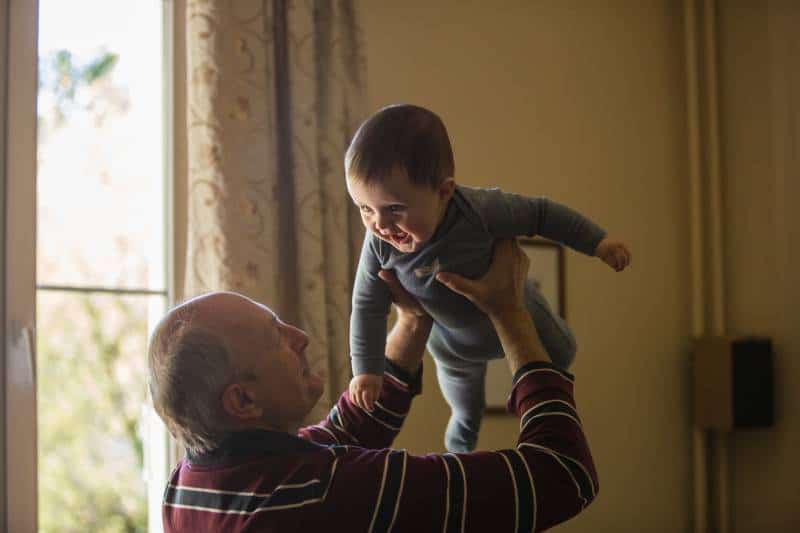 Un vieil homme tenant un bébé souriant à la maison