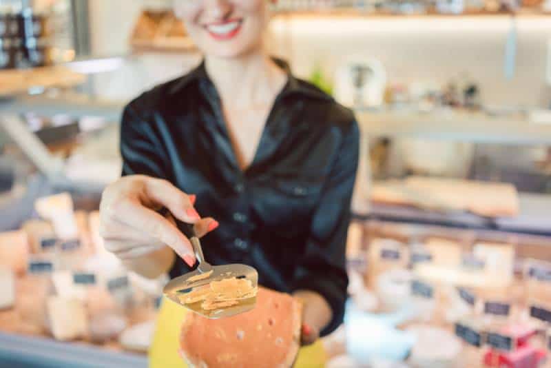Une belle femme offre du fromage sur un comptoir d'épicerie fine en coupant un bout de test
