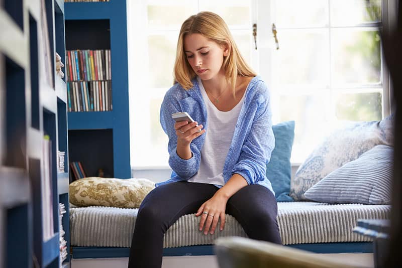 Une femme assise sur un canapé à la maison utilise un téléphone portable