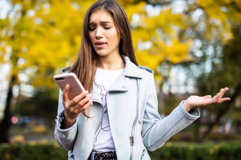 Une femme confuse regarde son téléphone dans un parc de la ville