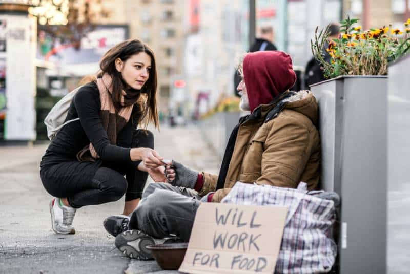 Une femme donne de l'argent à un sans-abri