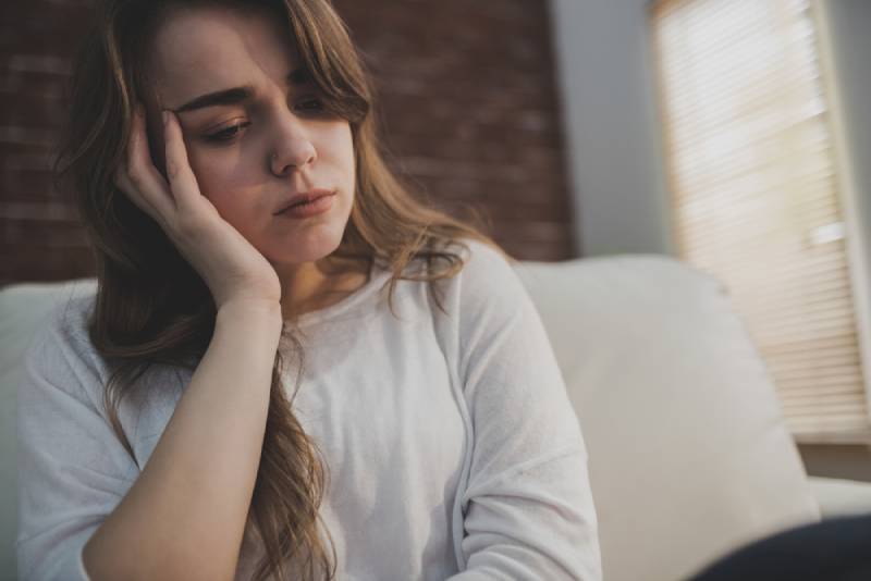 Une femme en colère assise sur le canapé et se tenant la tête dans le salon