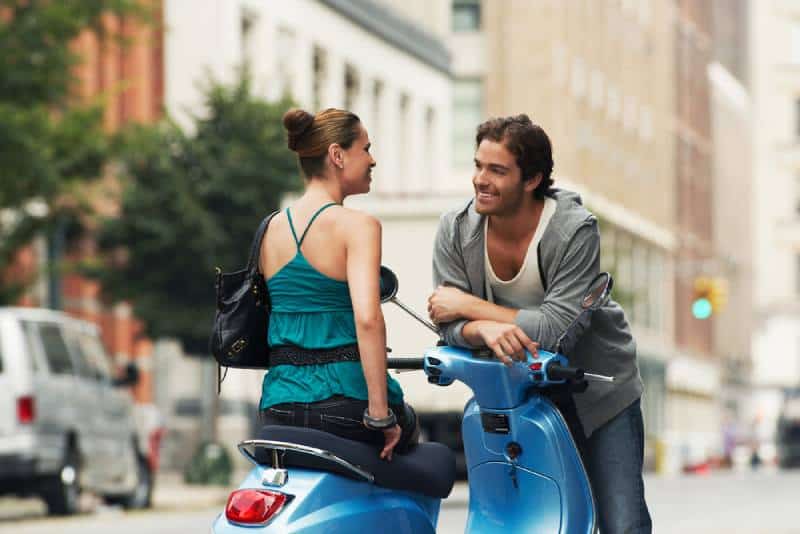 Une femme en mobylette parle à un homme dans la rue