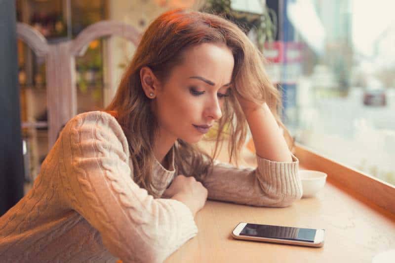 Une femme inquiète regarde son téléphone au café