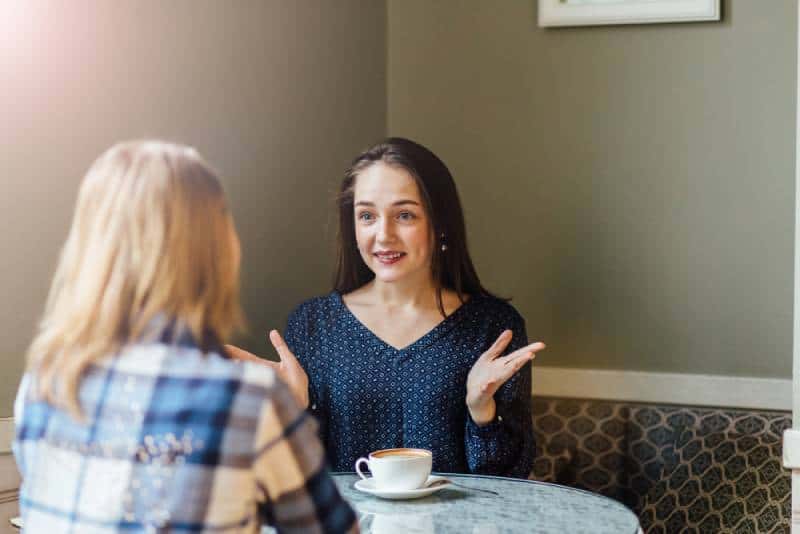 Une femme joyeuse partage la nouvelle avec son ami en buvant un cappuccino dans un café