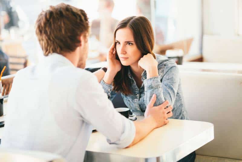 Une femme regarde l'homme de façon suspecte alors qu'il lui tient les bras dans un café