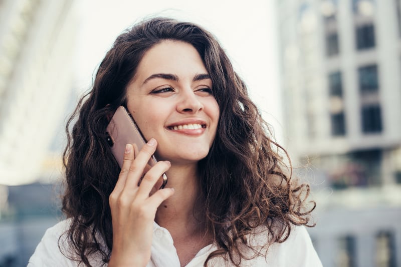 Une femme souriante qui parle au téléphone à l'extérieur
