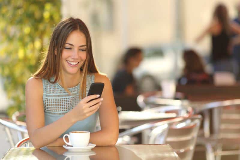 Une fille heureuse regarde son téléphone au café