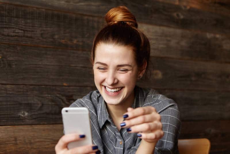 Une fille souriante regarde son téléphone au café