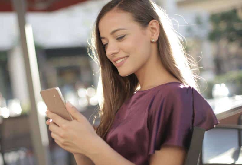 Une fille souriante tape au téléphone dans un café