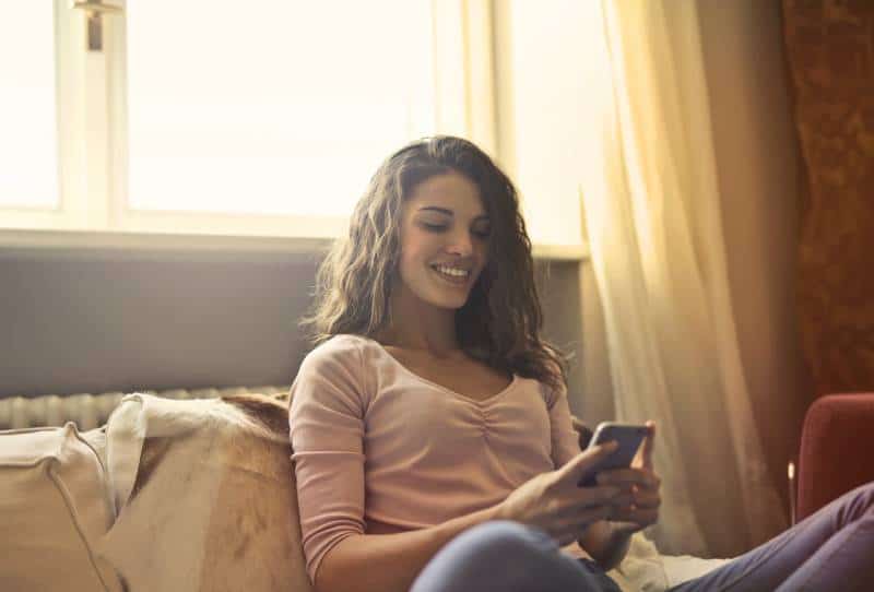 Une fille souriante tape sur son téléphone à la maison