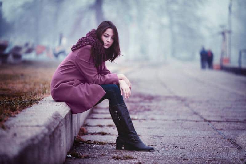 Une jeune femme décevante est assise sur le parapet de pierre en ce jour d'automne