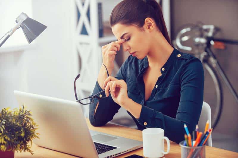 Une jeune femme frustrée garde les yeux fermés alors qu'elle est assise sur son lieu de travail au bureau