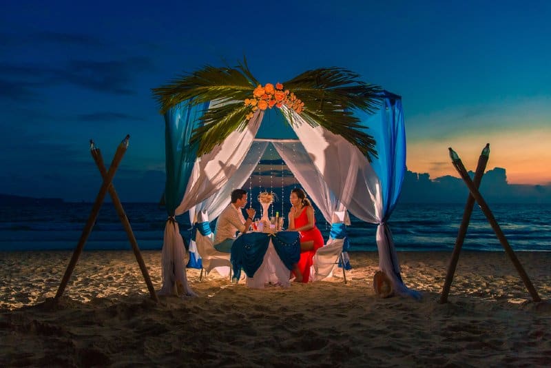 Jeune beau couple a un dîner romantique au coucher du soleil sur une plage tropicale