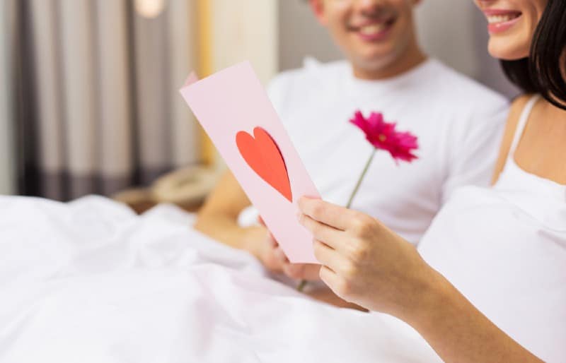 un couple heureux assis sur le lit avec carte postale et fleur