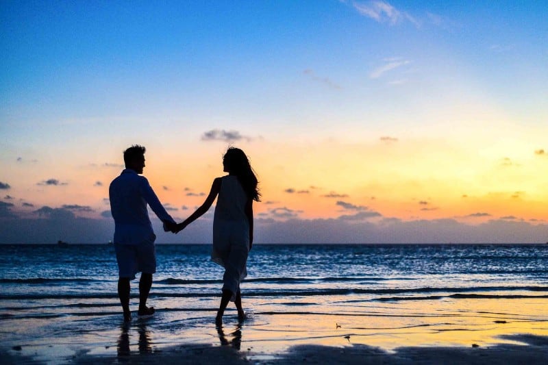 homme et main dans la main marchant sur le bord de mer au moment du coucher du soleil bord de mer
