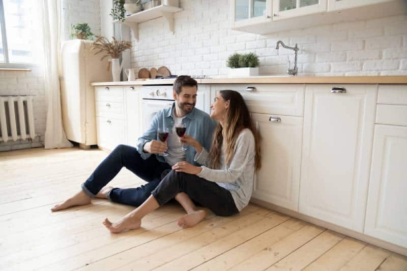 couple romantique assis sur le sol de la cuisine et buvant du vin tout en se regardant en souriant