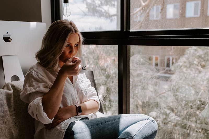 femme buvant du café à côté de la fenêtre à la maison