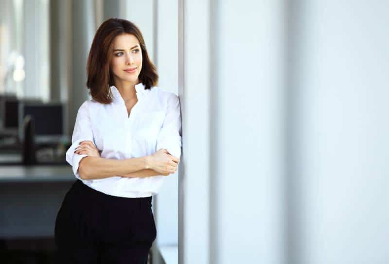 femme d'affaires en chemise blanche aux bras croisés, debout à côté de la fenêtre