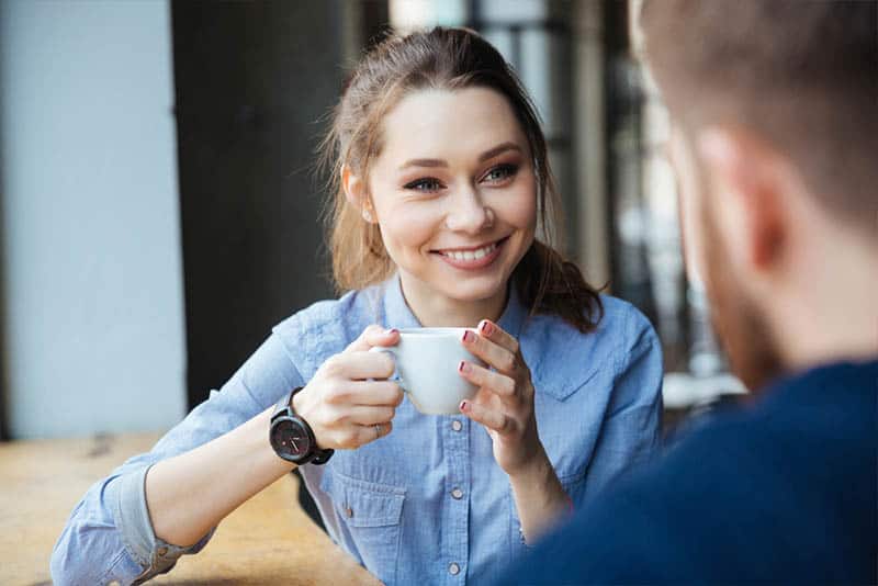 femme mignonne et souriante tenant une tasse de café et regardant un homme