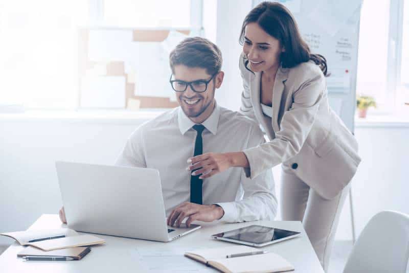 femme montrant son ordinateur portable en souriant avec son collègue de travail alors qu'elle est debout au bureau