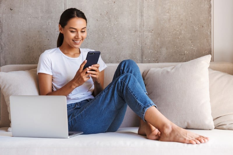 femme heureuse, assis sur le canapé, tenant un téléphone