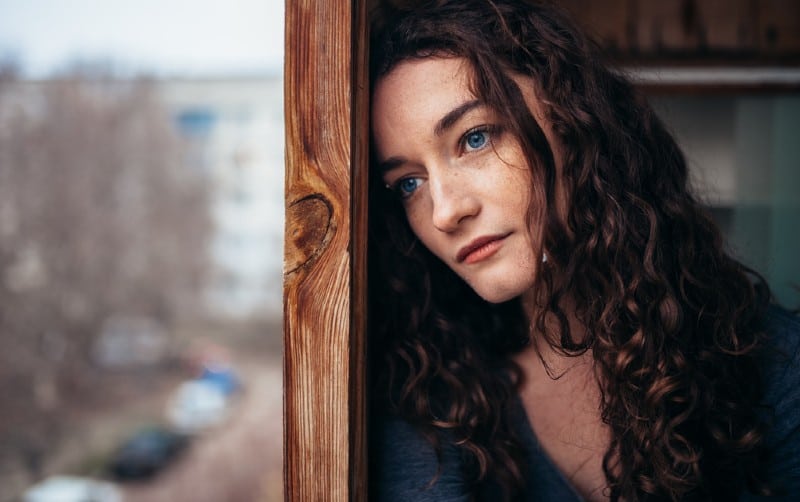 une triste femme brune debout près de la fenêtre