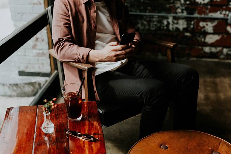 homme assis et tapant sur son téléphone dans un café pendant