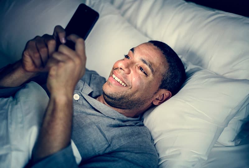homme en pyjama allongé sur le lit et tapant sur son téléphone