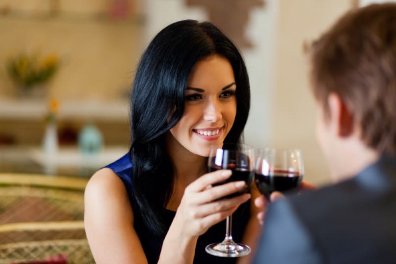 Un homme et une femme buvant du vin rouge assis l'un en face de l'autre à une table
