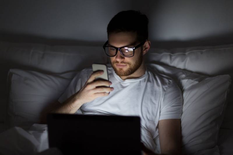 homme portant des lunettes et tapant sur son téléphone avant de dormir