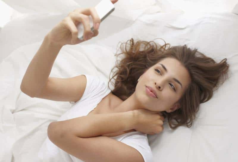 jeune brune allongée sur le lit et regardant son téléphone