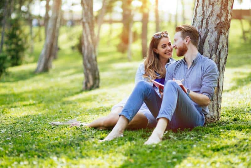joli couple assis sur l'herbe et appuyé sur un arbre