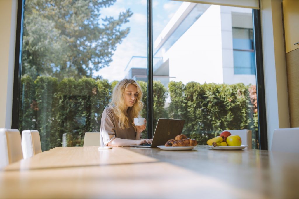 la femme est assise devant l'ordinateur portable et boit du café