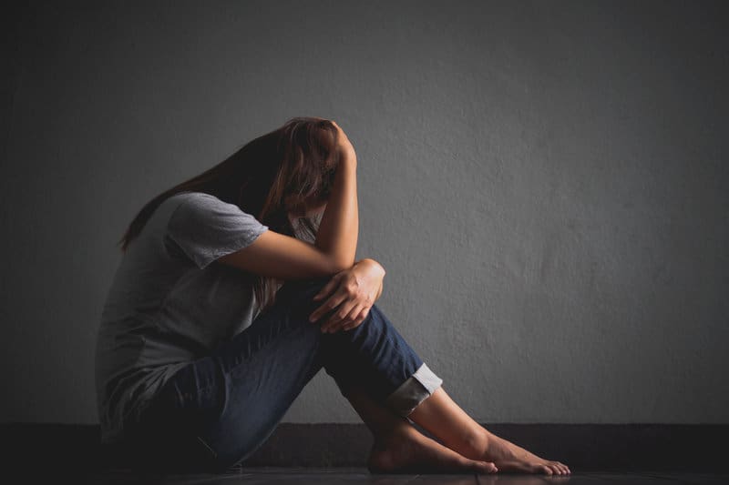 la femme est assise sur le sol, la tête baissée