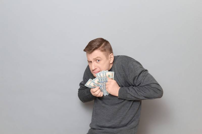 portrait d'un drôle d'homme mûr malheureux portant un pull, tenant un tas de dollars américains dans ses mains
