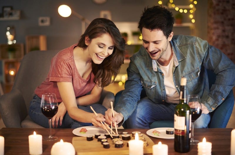 Un couple heureux de manger des sushis assis à une table avec du vin et des bougies dessus