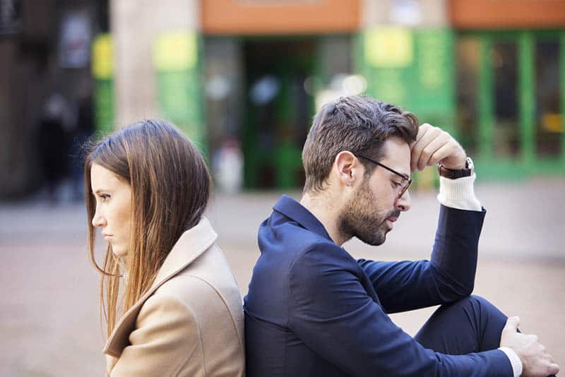 un homme et une femme bouleversés, assis dehors dos à dos